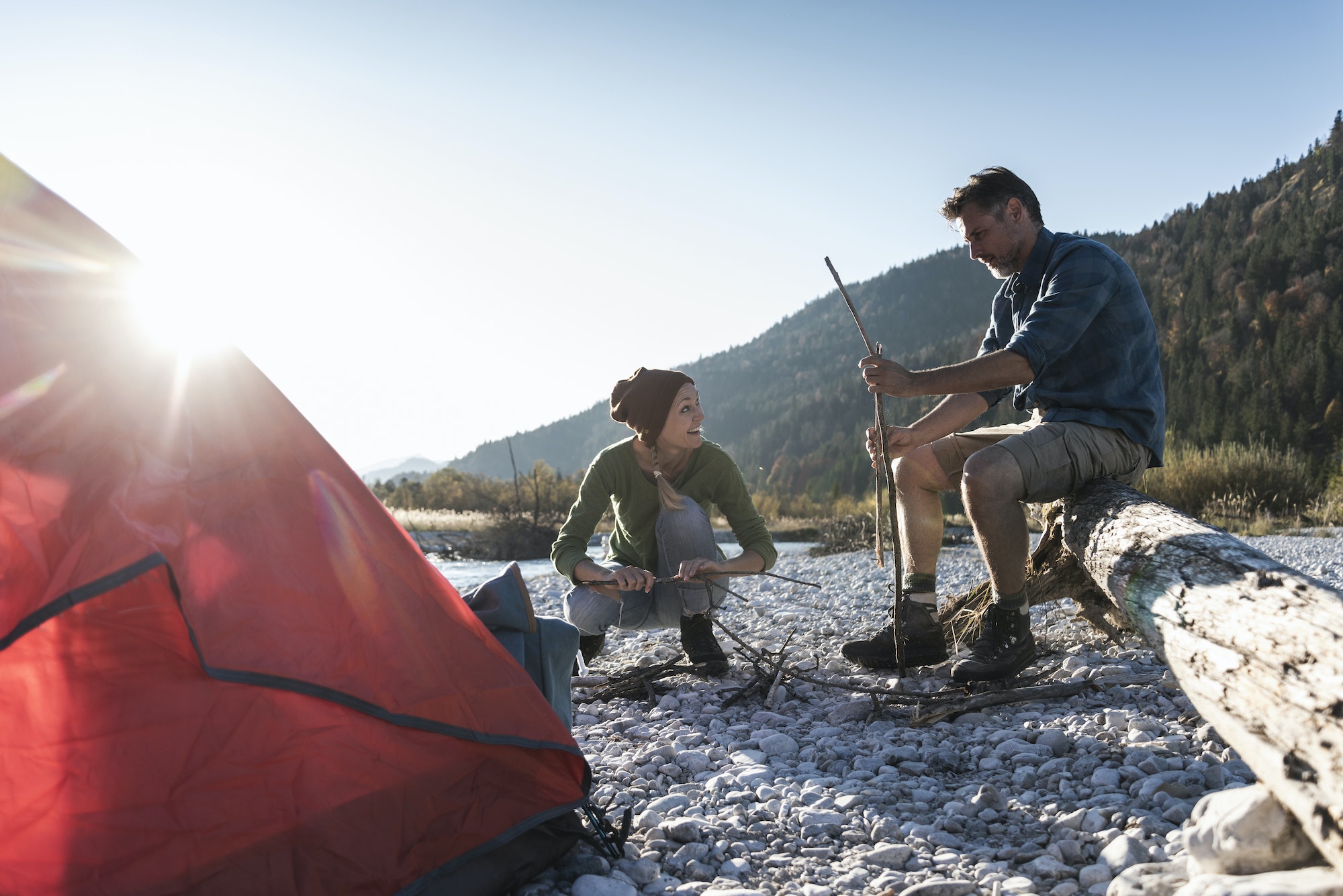 Mature couple camping at riverside, with wood for a camp fire